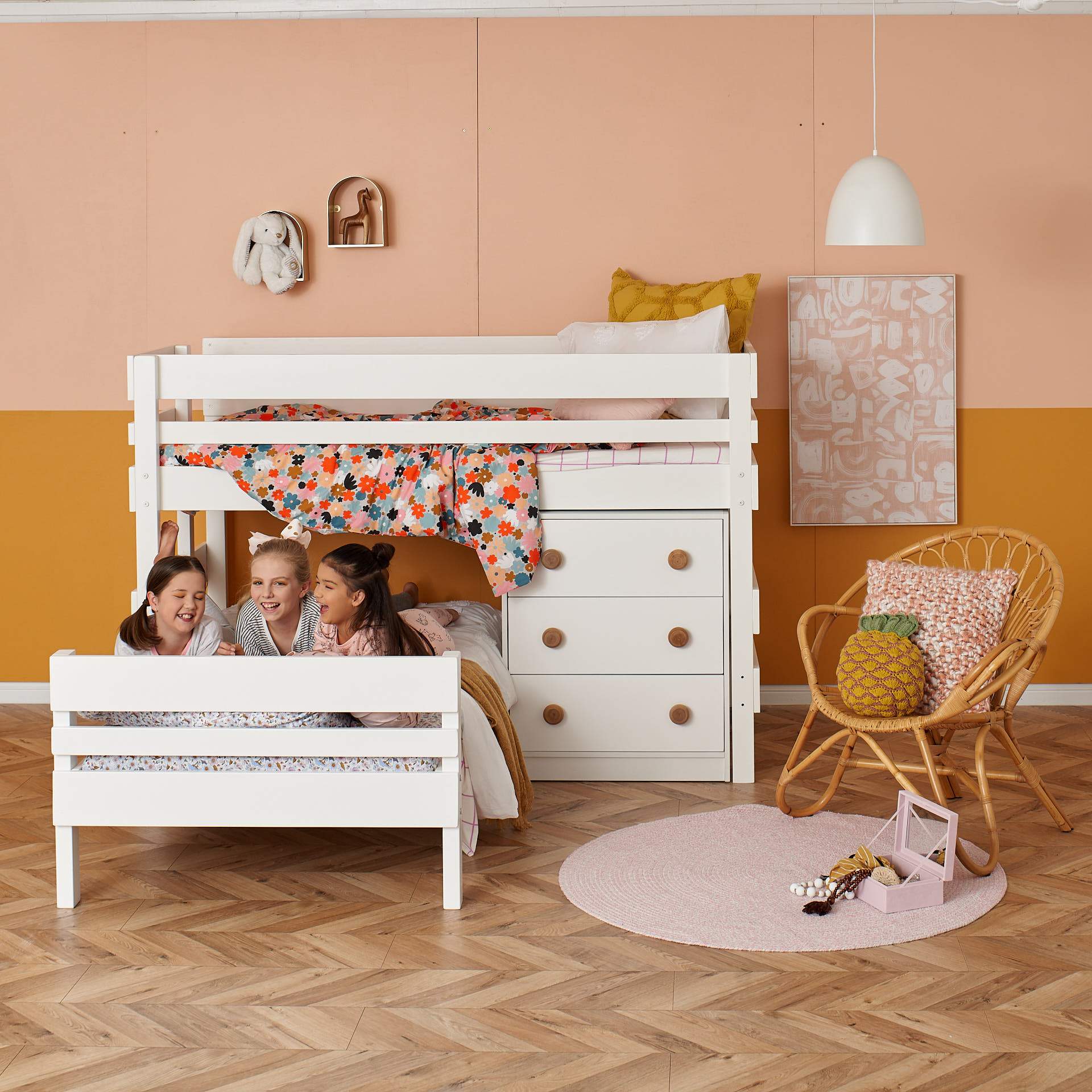 L shaped corner bunk bed with chest of drawers and 3 girls laughing on lower bed