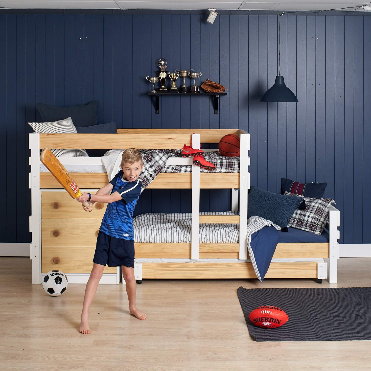 cricket playing kid in front of low height offset bunk bed with extra trundle bed sleeping space and deep drawer chest of drawers