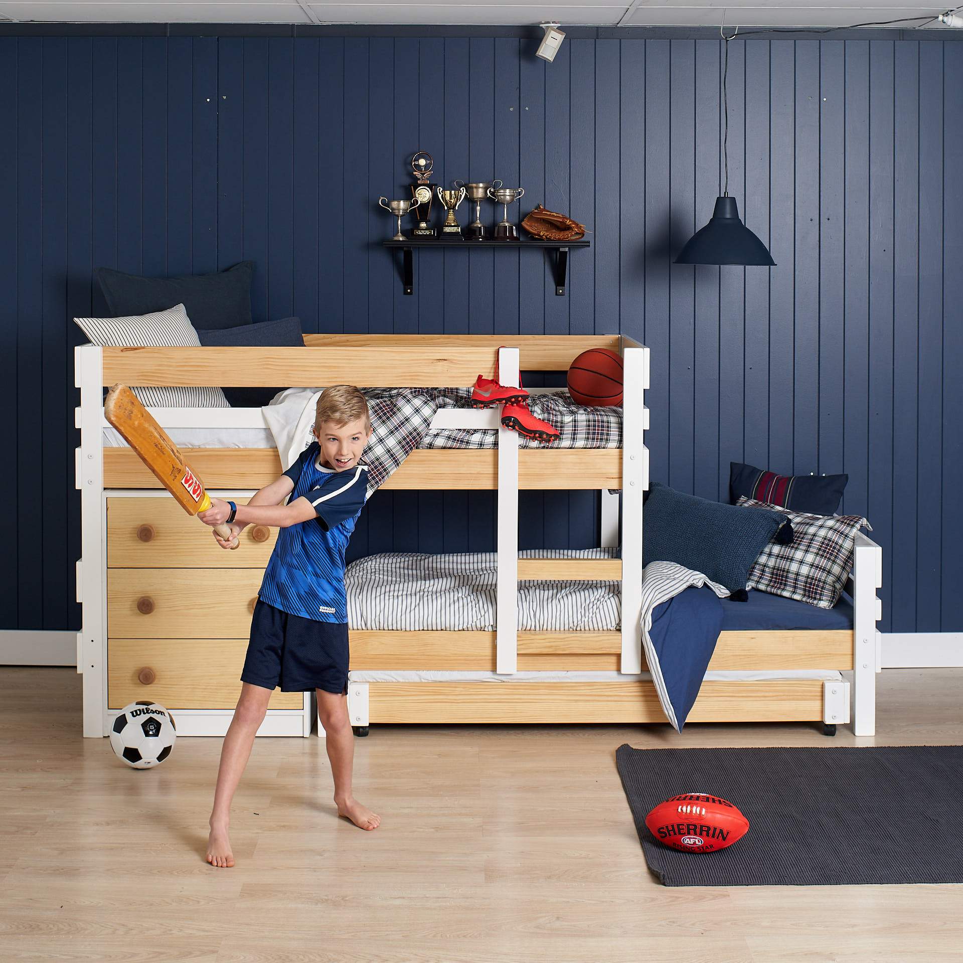 cricket playing kid in front of low height offset bunk bed with extra trundle bed sleeping space and deep drawer chest of drawers