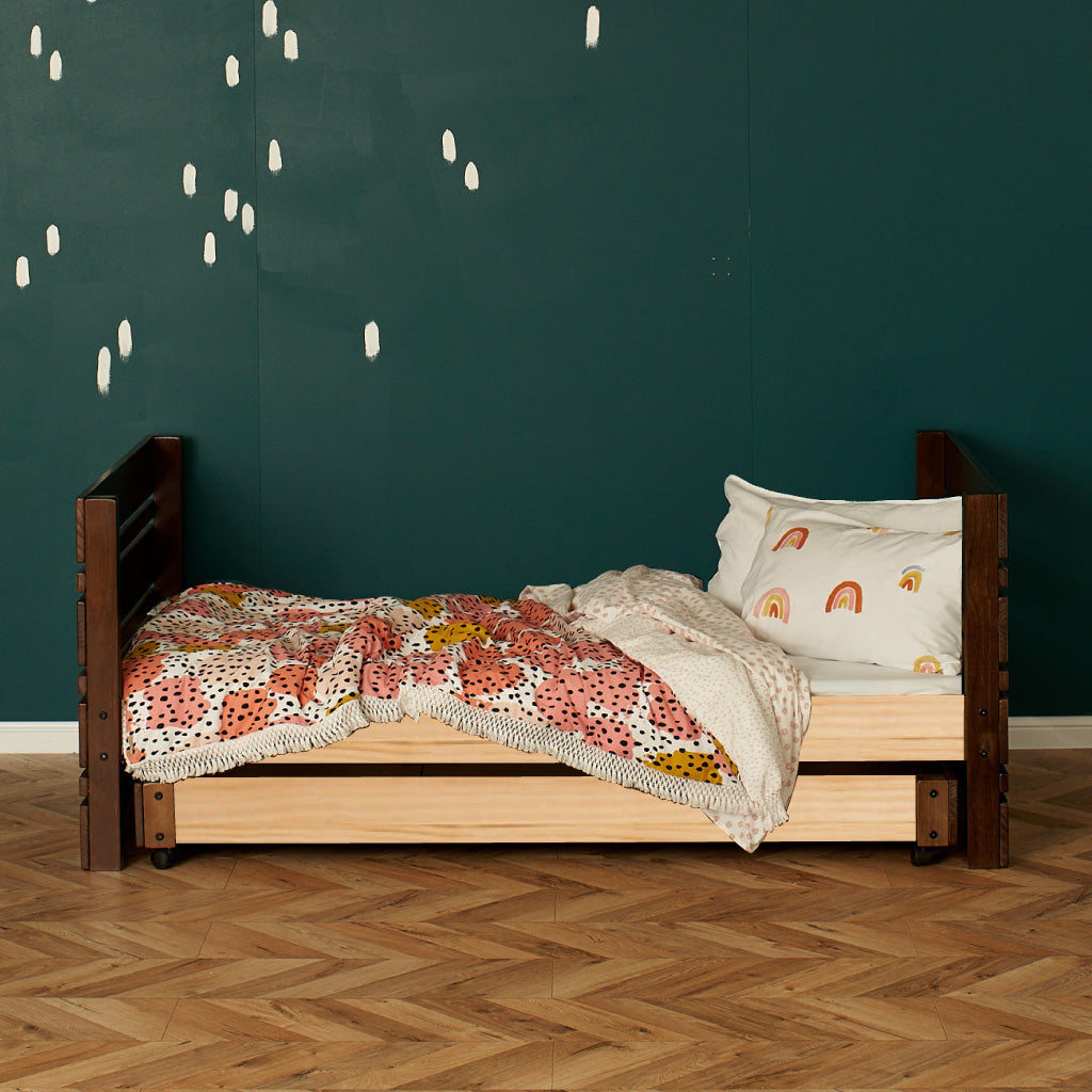 Native Elm captains bed with dark wood head and footboards, light wood frame, floral bedding, and rainbow pillow against.