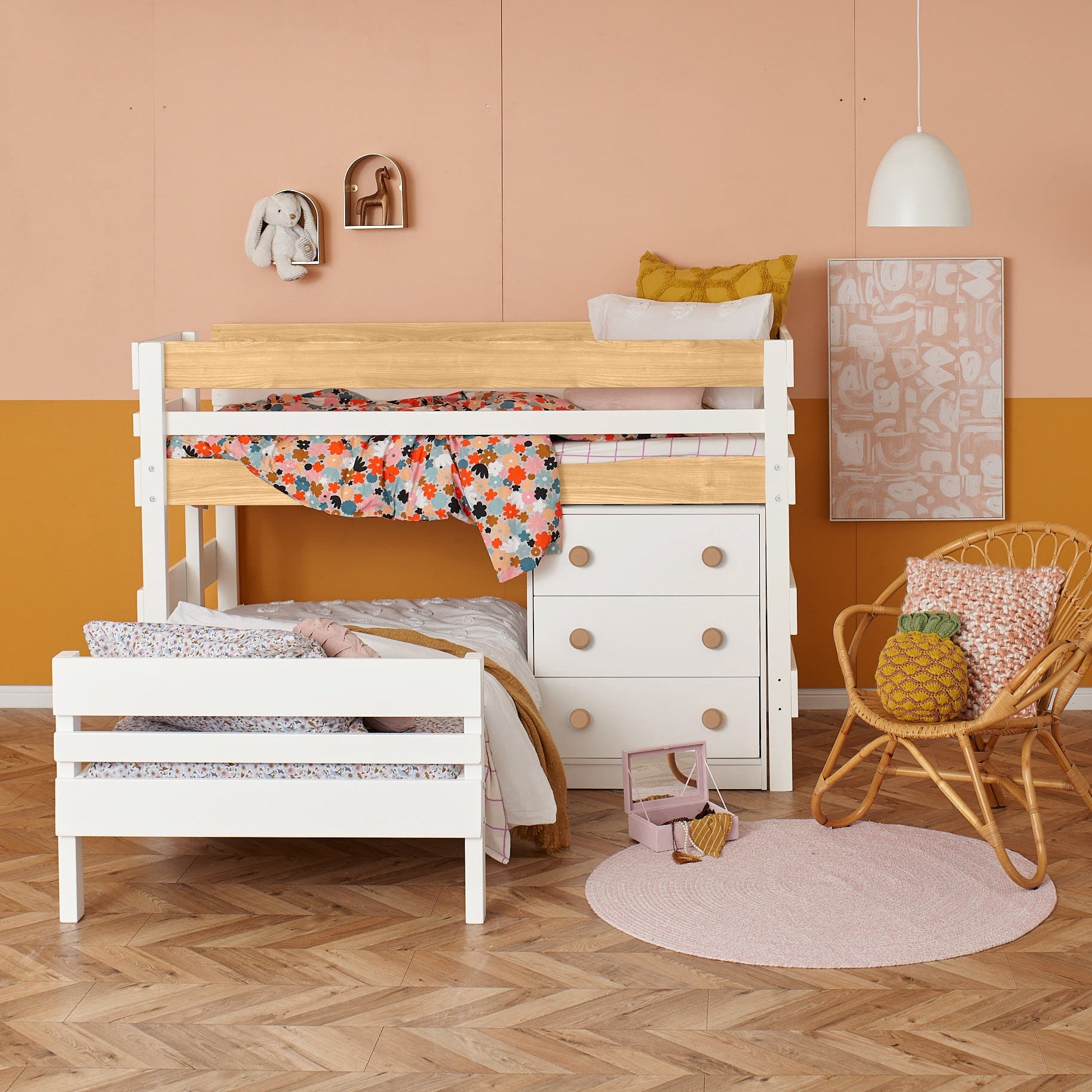 White low height corner bunk bed with wooden guardrails, colorful bedding, and integrated drawers beneath.