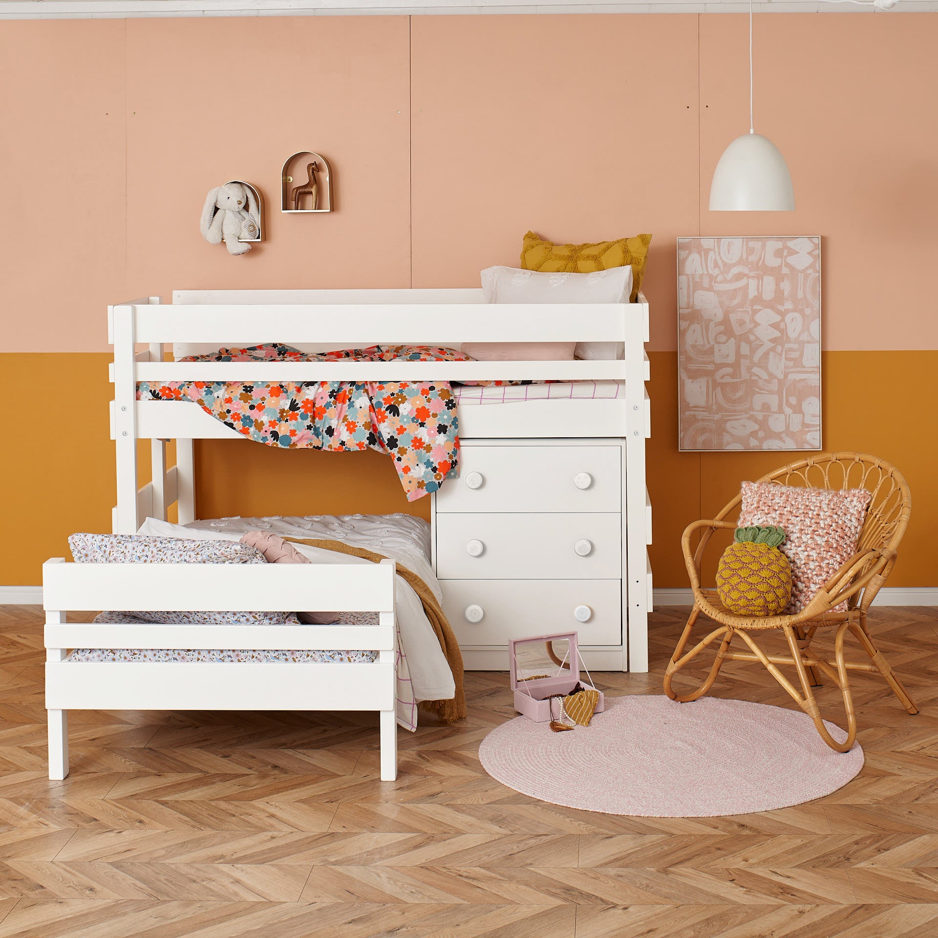 White low height corner bunk bed with floral bedding and built-in chest drawers in a warm, stylish room.