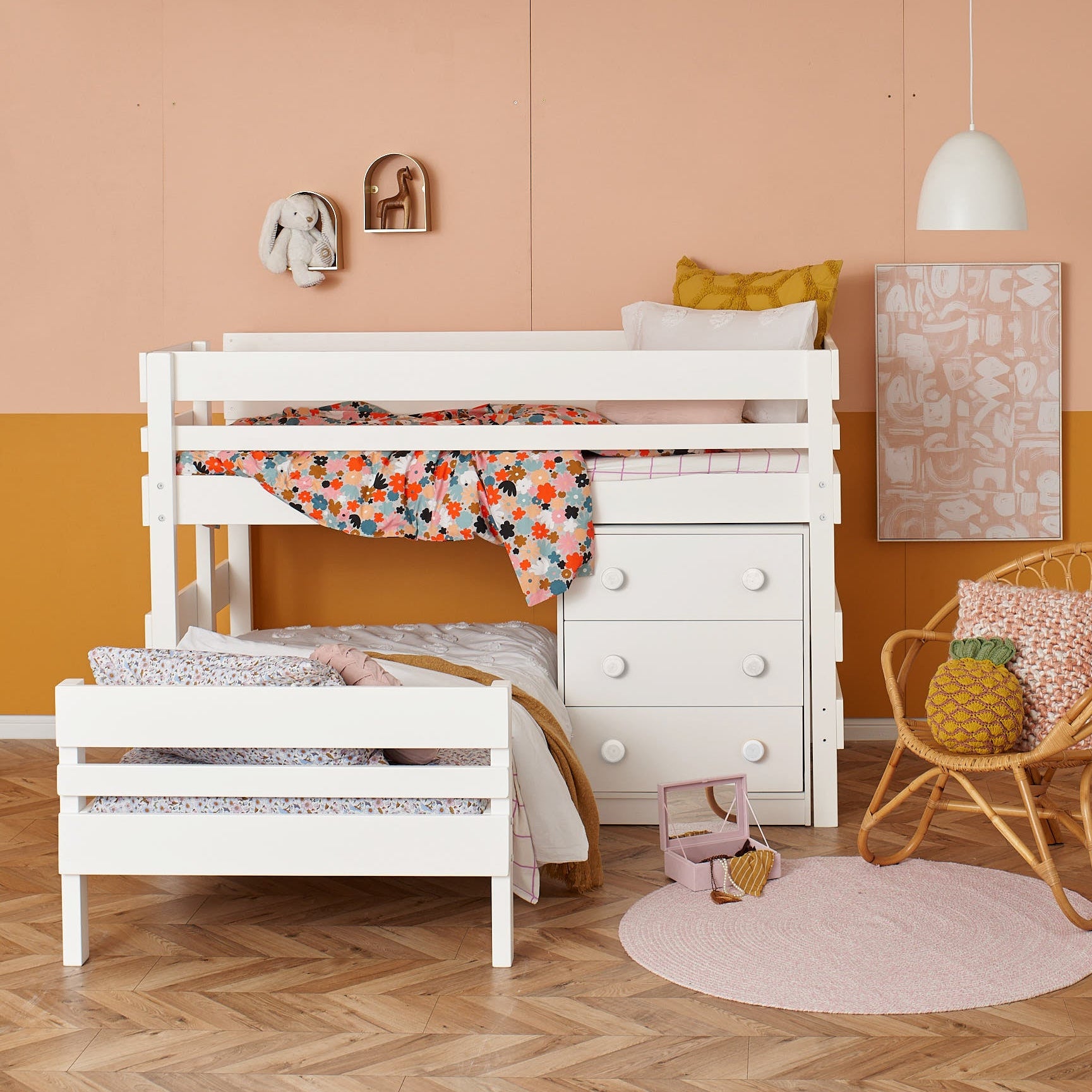 White low height corner bunk bed with floral bedding and built-in chest drawers in a warm, stylish room.