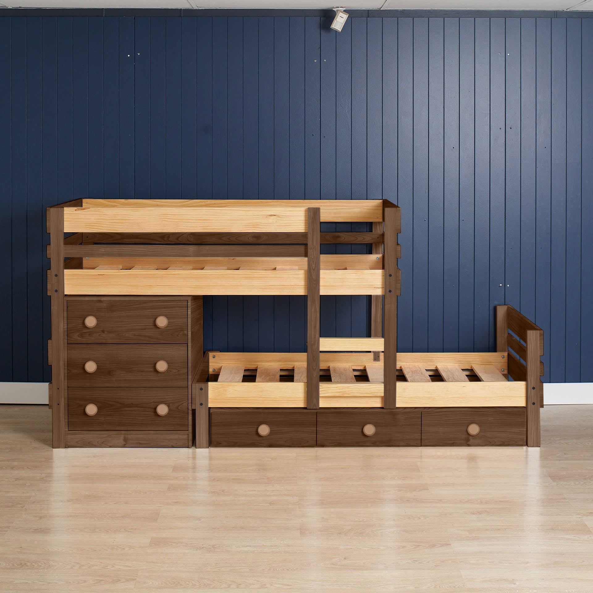 Low height long-wall bunk bed in elm wood with integrated chest drawers and slide-out trundle bed on light floor and blue.