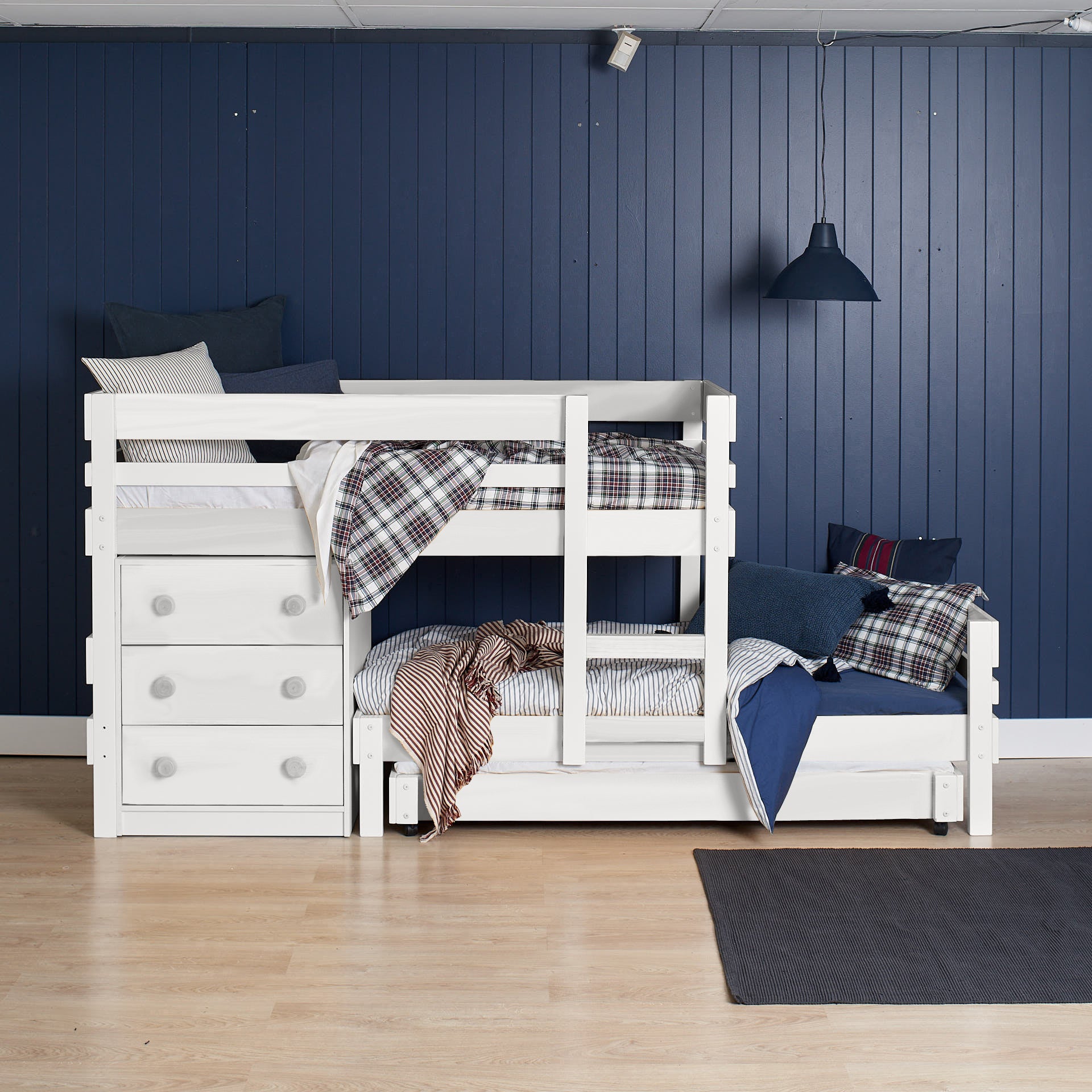White low height long-wall bunk bed with built-in chest drawers and ladder against navy paneled wall.