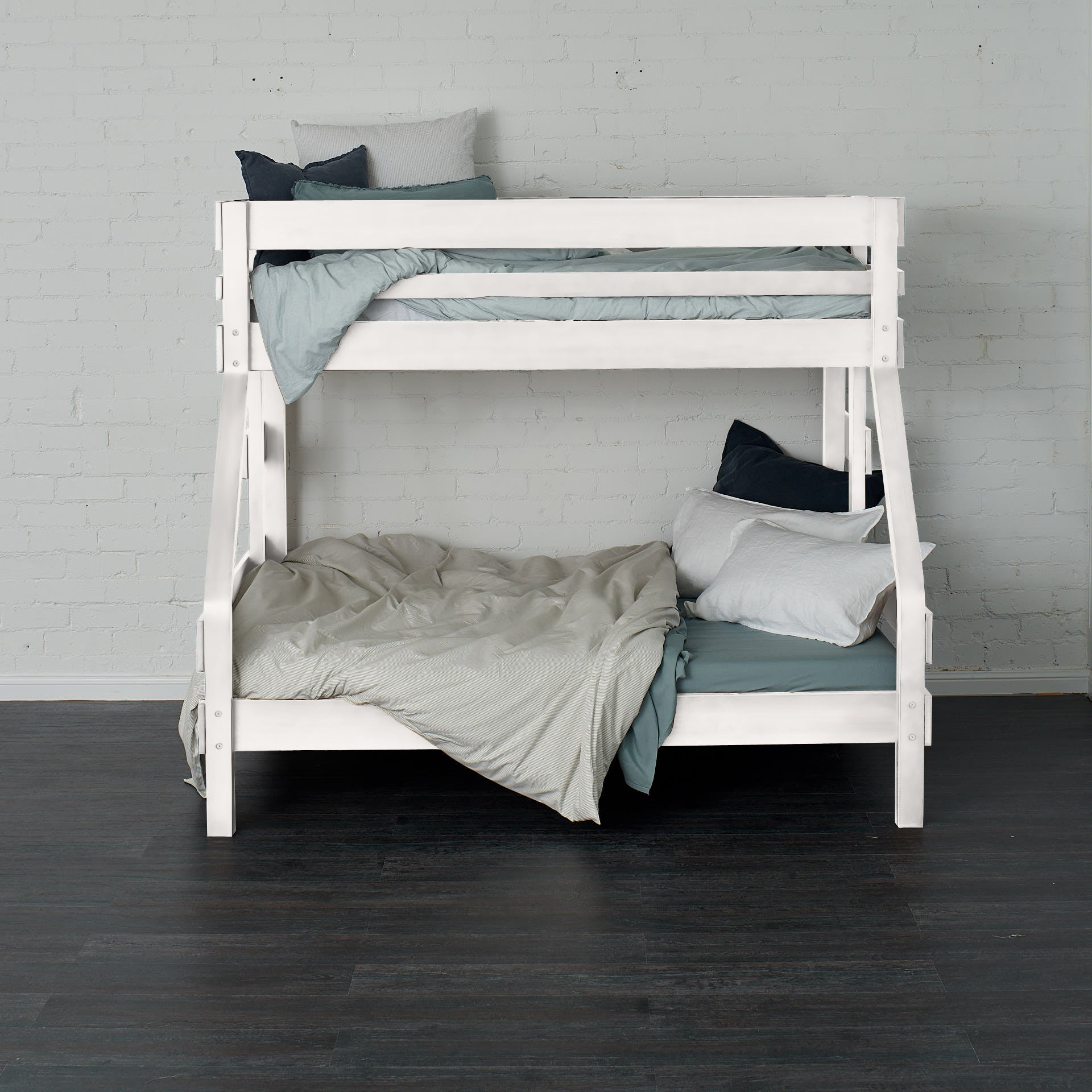 White single over double bunk bed with ladder and bedding against white brick wall.