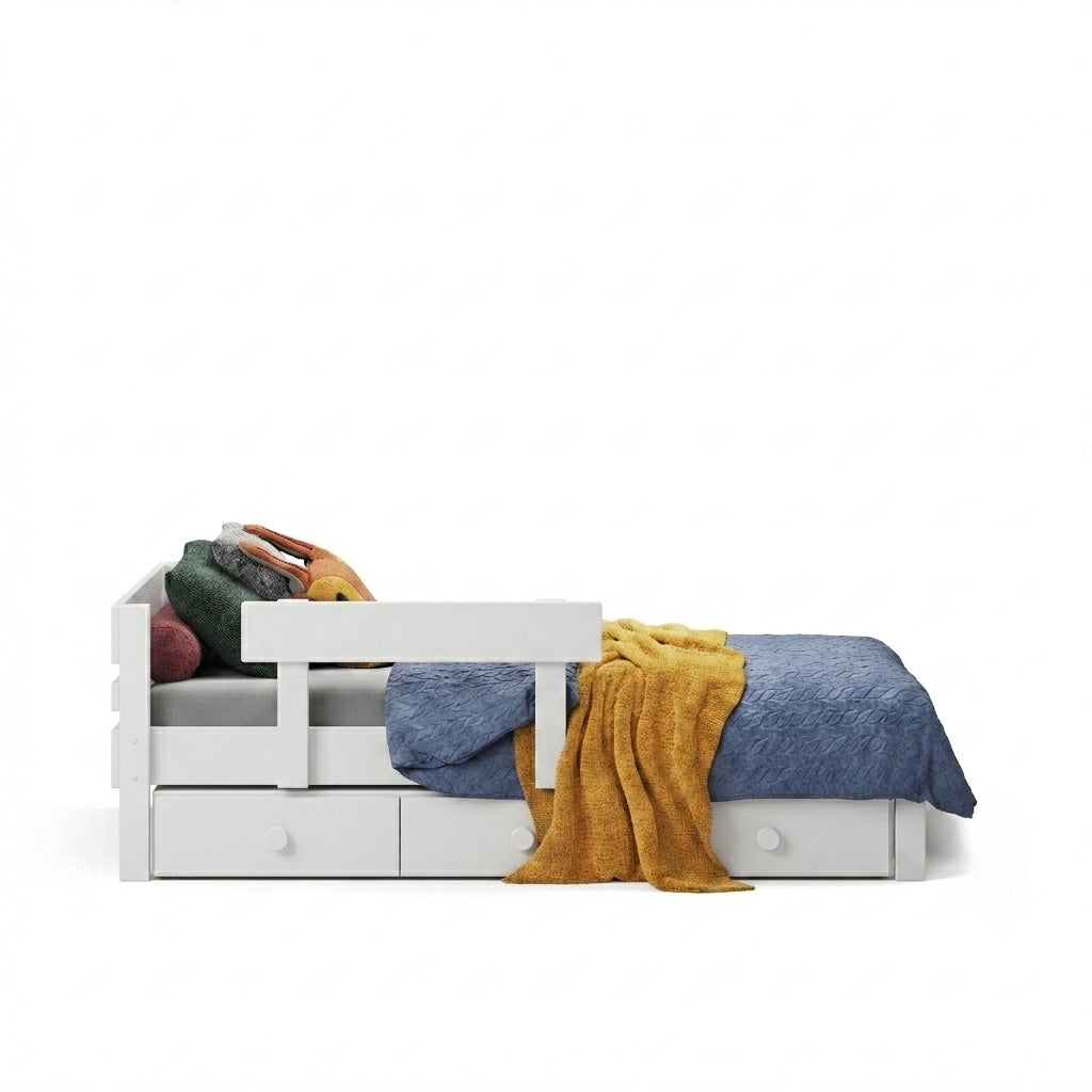 A white wooden bed with matching safety rail and under bed storage drawers. Styled with a blue textured blanket, a mustard yellow throw, and colorful pillows.