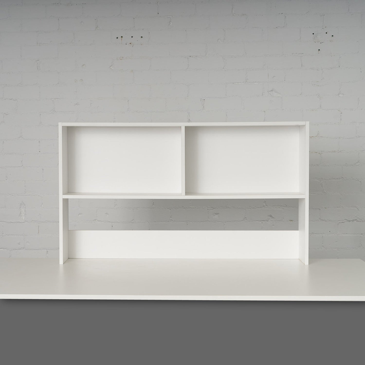 Minimalist white Bench Bookcase with two open compartments against a light brick wall background