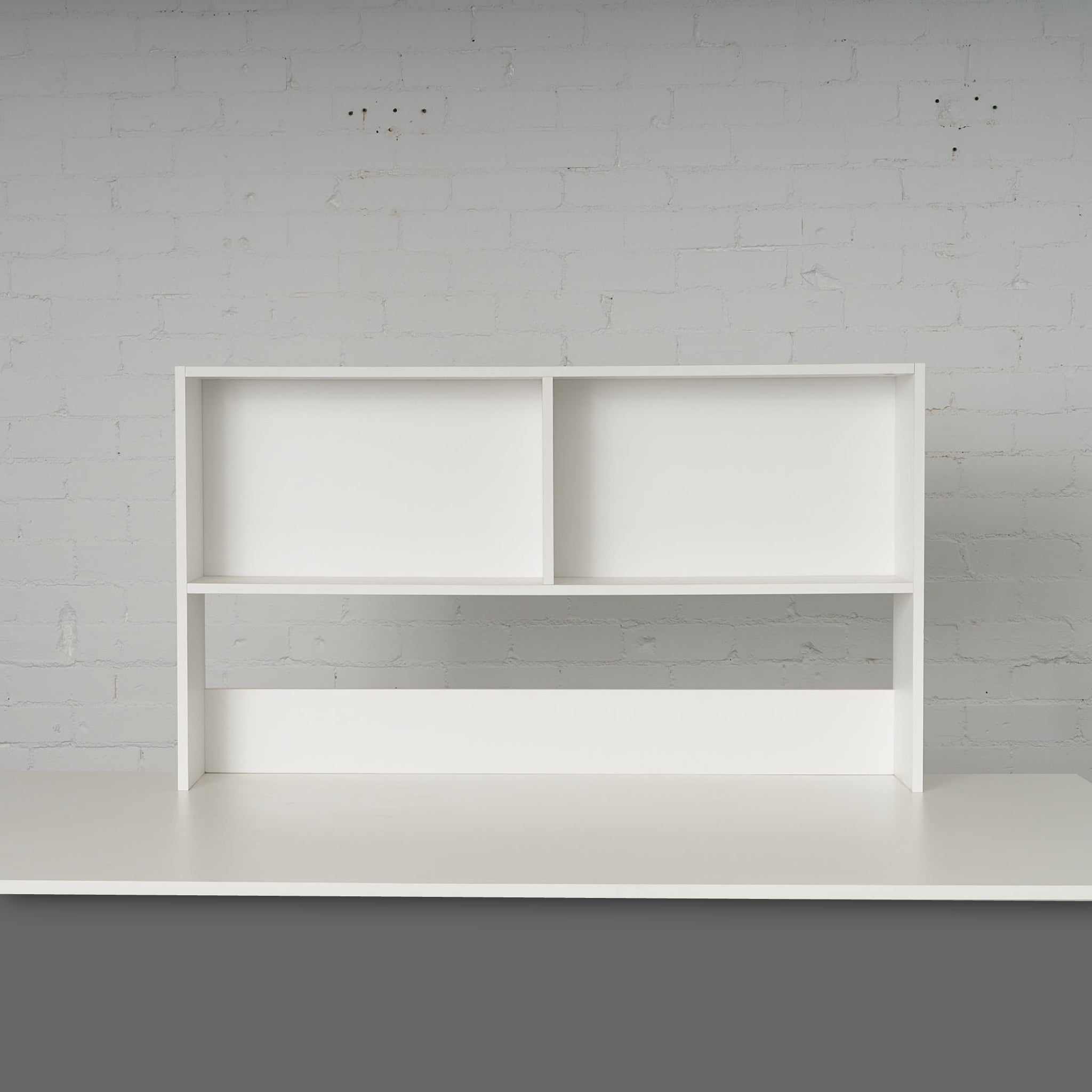 Minimalist white Bench Bookcase with two open compartments against a light brick wall background