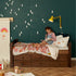 Child reading on a Captain Bed with wooden frame, drawers, colorful bedding, and dark green wall background.