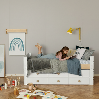 White captain’s bed with three under-bed drawers, styled with gray and blue bedding and a yellow wall lamp.