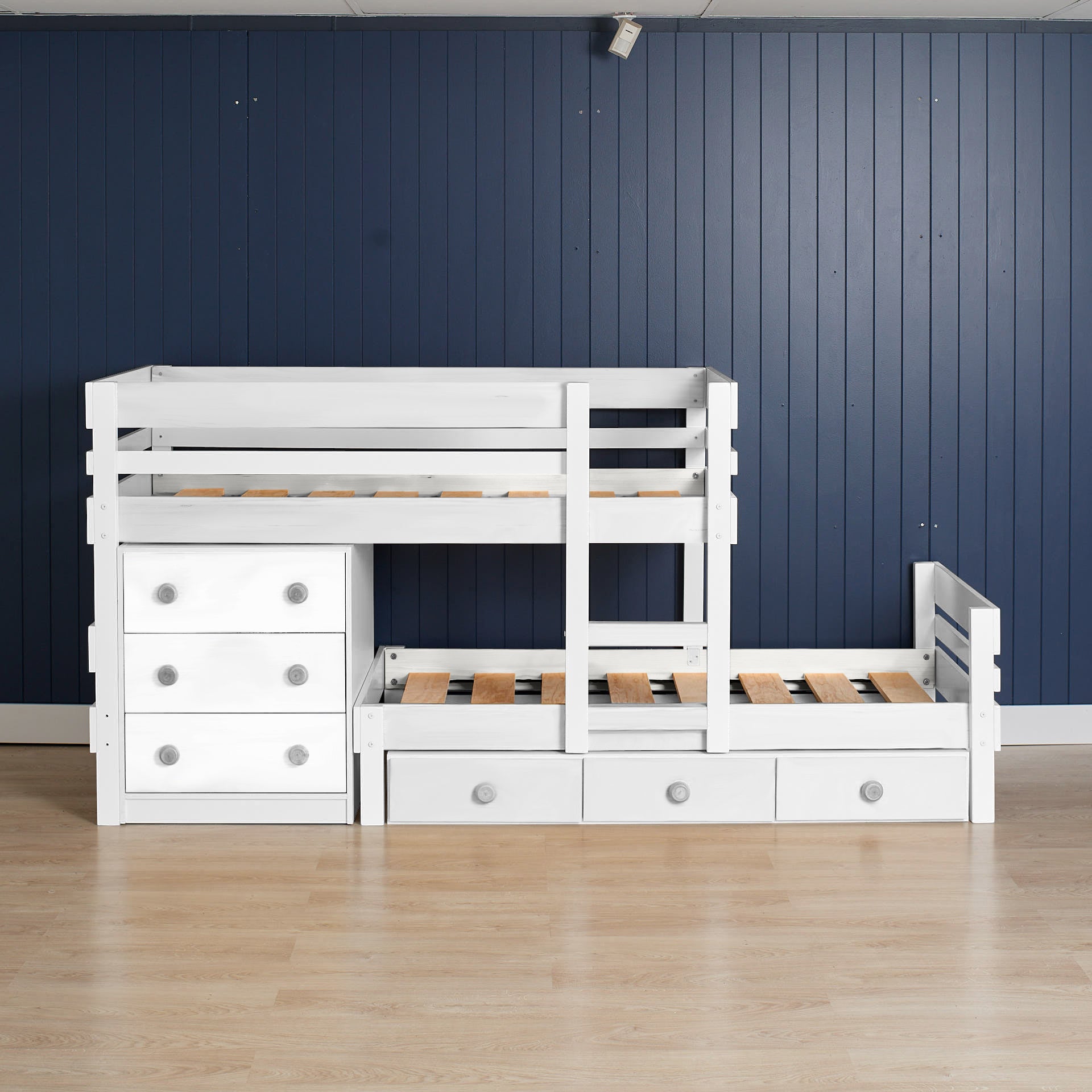 White low height long-wall bunk bed with integrated chest drawers and pull-out drawer storage on wooden floor.