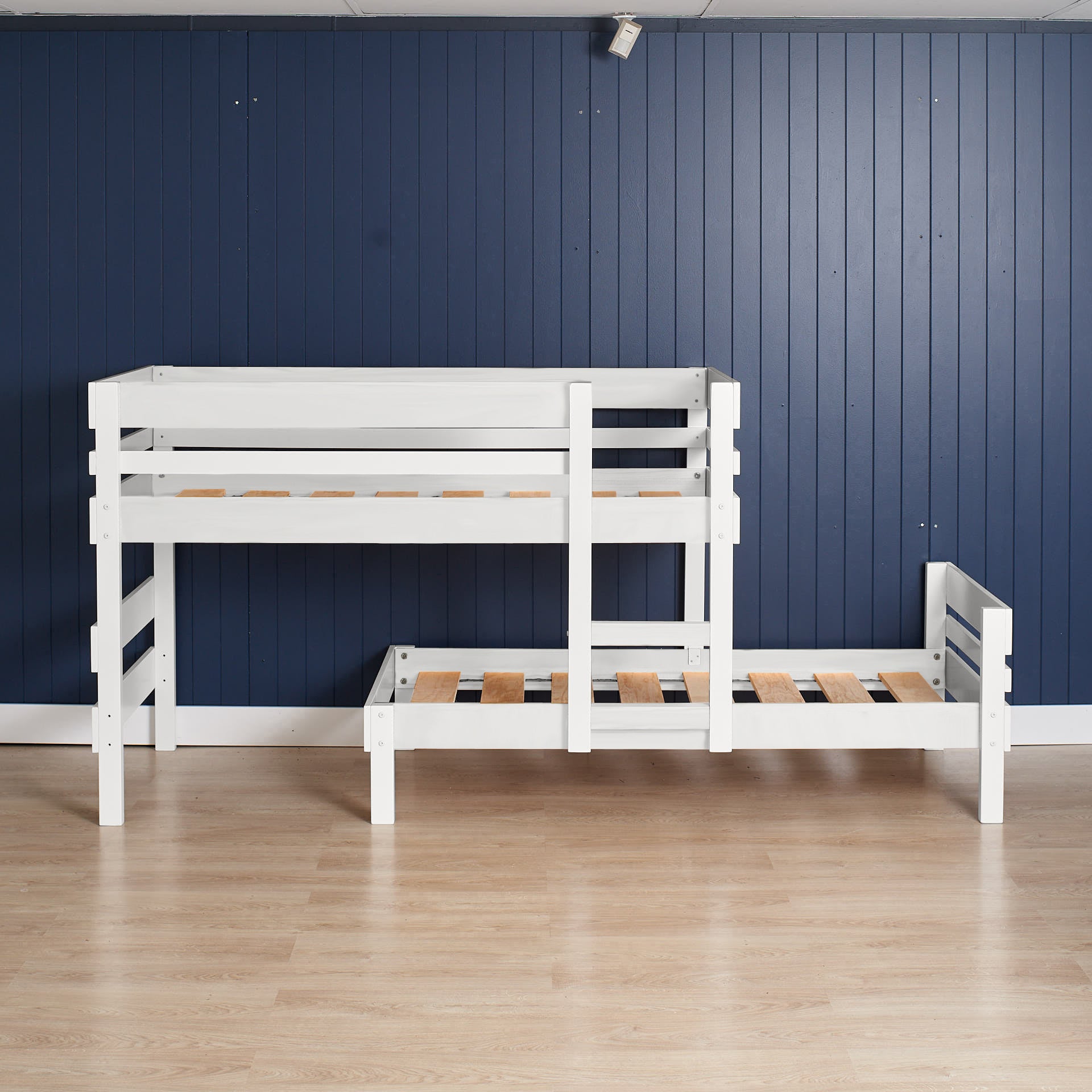 White low height long-wall bunk bed with slatted guardrails and integrated stairs on light wood floor.