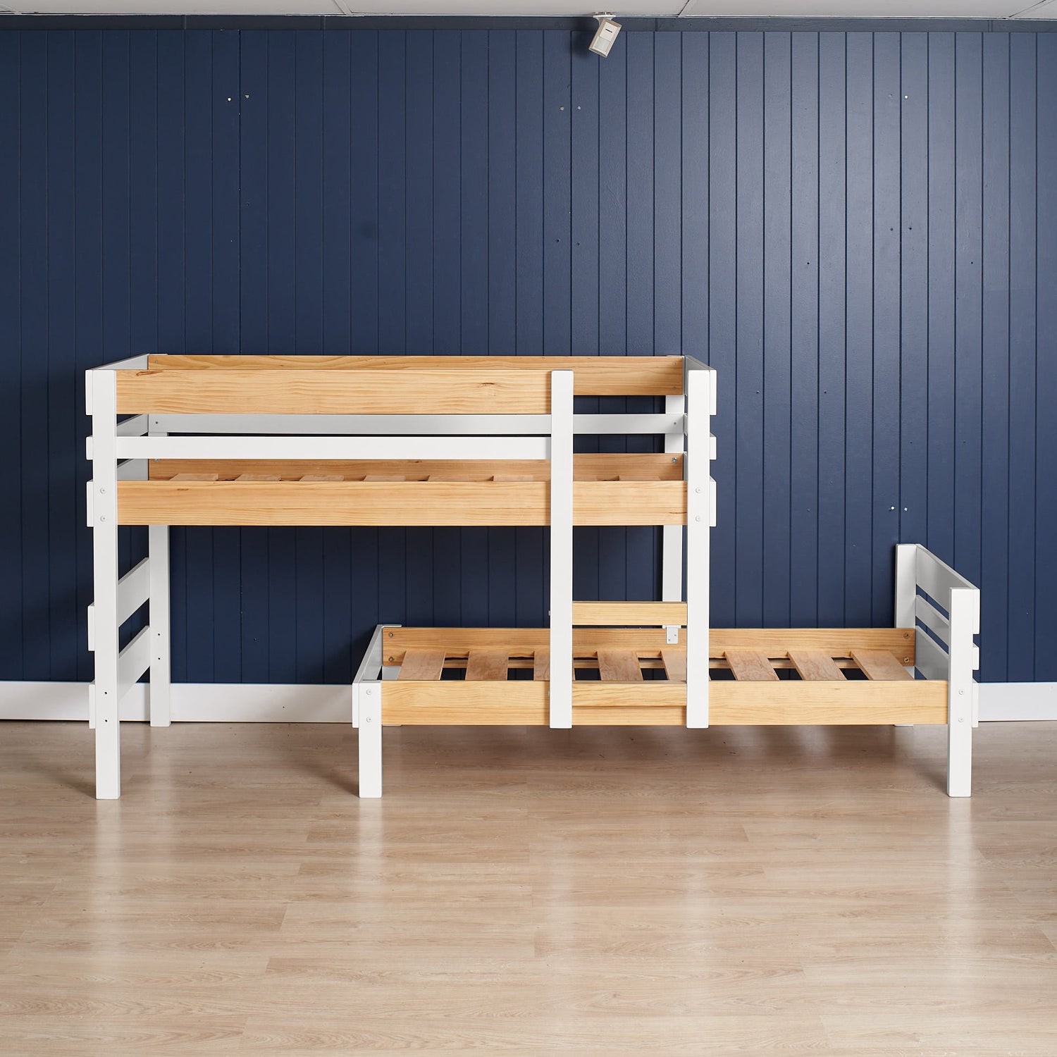 Low height long-wall bunk bed in white and natural elm with guardrails and ladder on light wood floor.