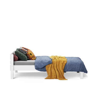 White single bed with slatted headboard, blue bedding, mustard throw, and multiple pillows.