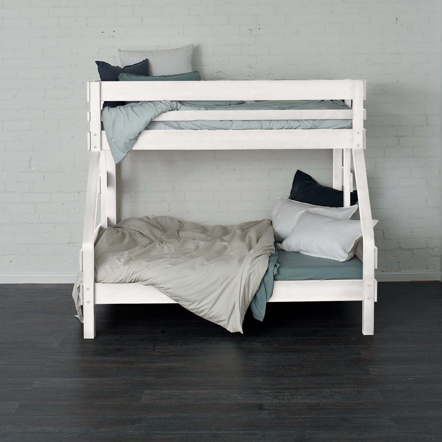 White single over double bunk bed with ladder and bedding against white brick wall.