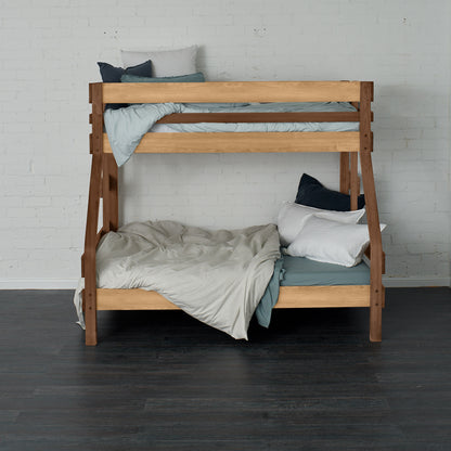 Native elm single over double bunk bed with ladder, soft grey bedding, and pillows.
