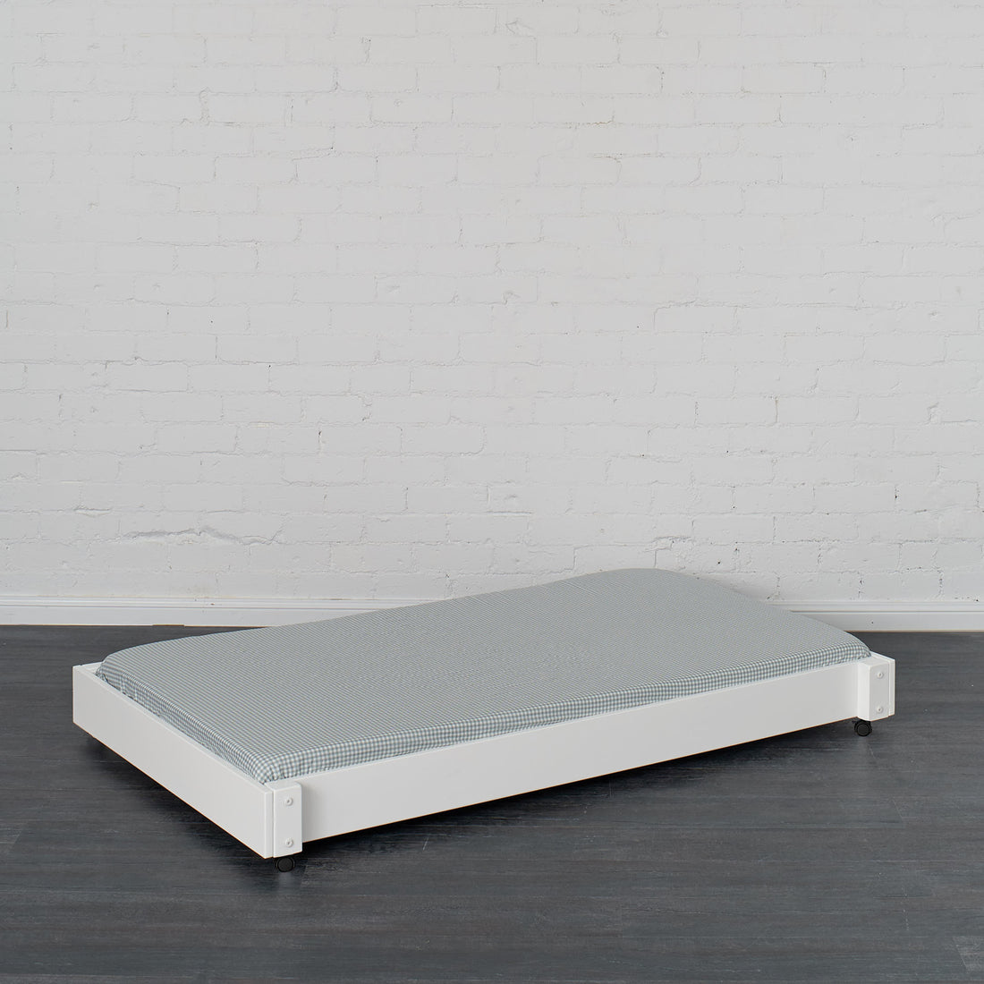 White trundle bed with low profile frame and gray mattress on dark wood floor.