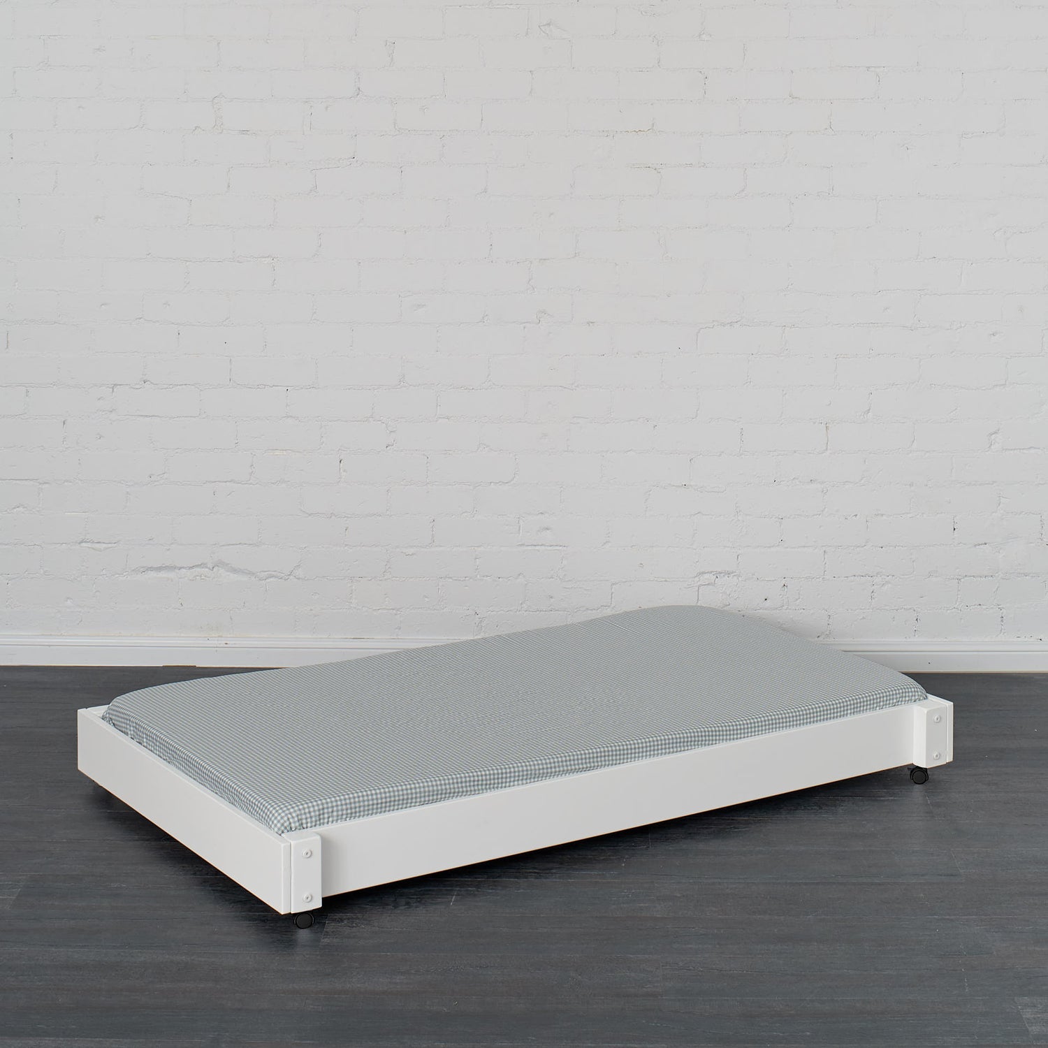 White trundle bed with low profile frame and gray mattress on dark wood floor.