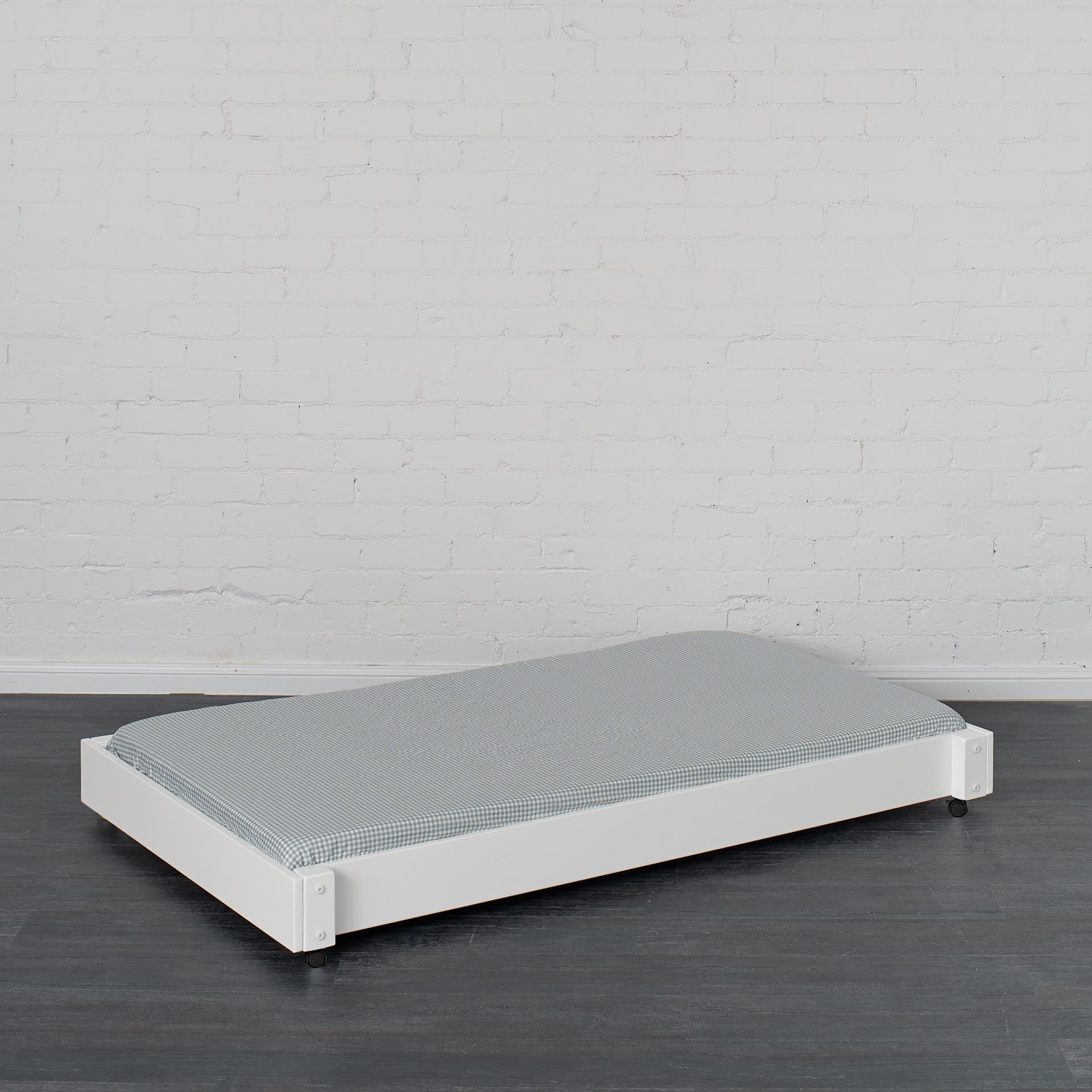 White trundle bed with low profile frame and gray mattress on dark wood floor.