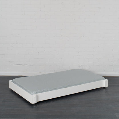 White trundle bed with low profile frame and gray mattress on dark wood floor.