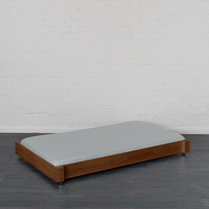 Low wooden trundle bed in natural elm finish with simple slatted base and gray mattress.